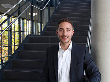 Portrait Prof. Dr. Nils-Ole Hohenstein vor einer Treppe innerhalb des DHBW-Mannheim-Gebäudes in der Coblitzallee