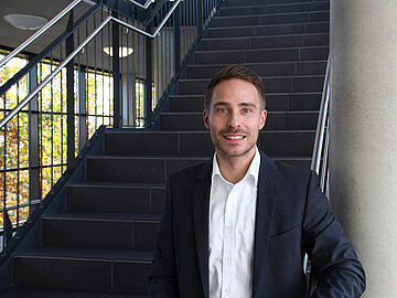 Portrait Prof. Dr. Nils-Ole Hohenstein vor einer Treppe innerhalb des DHBW-Mannheim-Gebäudes in der Coblitzallee