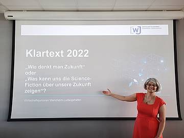 Eine Frau mittleren Alters deutet auf ihre Vortragspräsentation zum Thema: Wie denkt man Zukunft oder Was kann uns Science-Fiction über unsere Zukunft sagen?