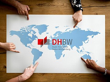 Weißes Blatt mit Umriss Weltkarte in hellblau, in der Mitte das DHBW-Logo. Fünf Hände, die ins Bild reinragen und auf fünf unterschiedliche Stellen auf der Weltkarte zeigen. 
