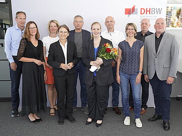 Gruppenbild mit 10 Personen, eine Dame vorne in der Mitte mit Blumen in der Hand. 