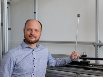 Porträt Prof. Johannes Börner mit seiner linken Hand auf einem inversen Pendel, Blick in die Kamera. 