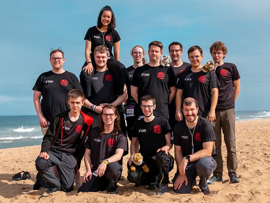 12 Team-Mitglieder der TIGERs am Strand, im Hintergrund das Meer.