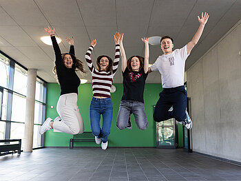 Foyer in der Dualen Hochschule Mannhim mit grüner Wand: 4 Studierende springen freudestrahlend hoch