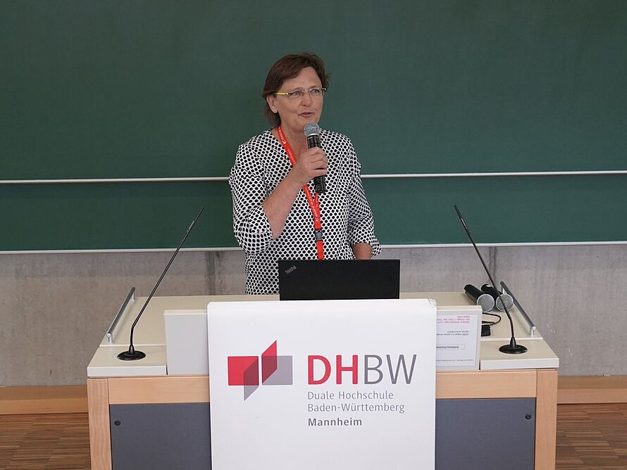 Frau mit Mikrofon an Redepult spricht zu Plenum