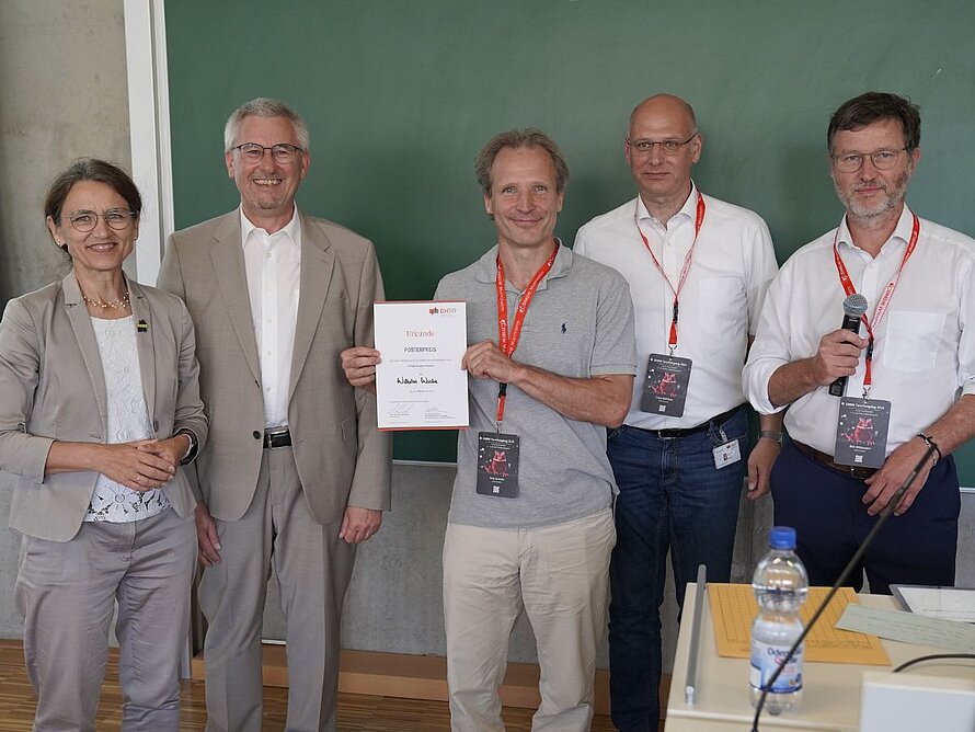 Gruppenbild mit 5 Menschen. Ein Mann in der Mitte hält eine Urkunde. 