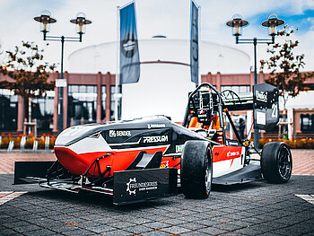 Elektrischer Rennwagen in rot und schwarz vor einem Gebäude.