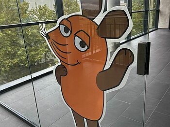 Glastür in der DHBW Mannheim, auf der eine 1 Meter hohe WDR-Maus klebt.   