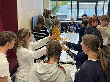 16 Schüler*innen im Alter zwischen 12 und 18 Jahren, die mit Spaghetti und Marshmallows Türme bauen. 