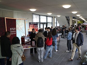 Blick ins Foyer des D-Gebäudes mit vielen Menschen an mehreren Infoständen - im Vordergrund der Stand der Studierendenvertretung. 