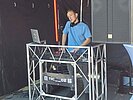 DJ Nic OZ steht beim Ersti-Welcome der DHBW Mannheim an seinem DJ-Pult mit Laptop und Mischpult. Um ihn herum stehen Lautsprecher und Veranstaltungstechnik. 