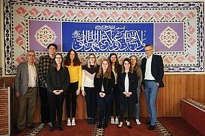 International-Business-Studierende der DHBW Mannheim in der Mannheimer Moschee vor einer von Kalligrafien geschmückter Wand. 