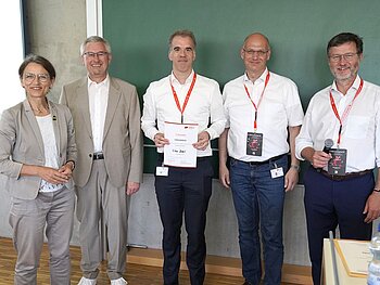 Gruppenfoto mit 5 Personen vor einer Tafel, Herr Prof. Zippel mit Urkunde in der Mitte.  