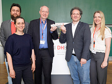 Gruppenbild mit 5 Personen in einem Hörsaal der DHBW Mannheim; symbolisch wird ein Staffelstab von einem Mann zum nächsten übergeben. 