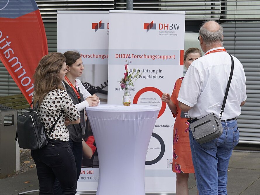 4 Menschen an Stechtischen im Austausch auf dem Hof der DHBW Mannheim
