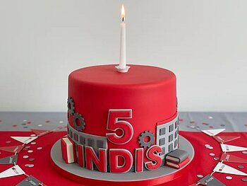 Eine rote Torte mit Kerze darauf sowie den Schriftzug INDIS und einer 5. 