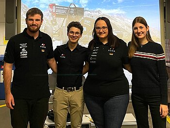 Gruppe mit 4 Studierenden dahinter auf einer Präsentation das Bild des Rennwagens in der Schweiz.