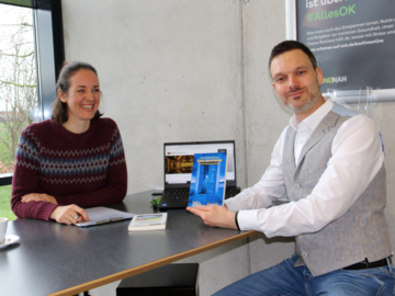 Julia Barisic an einem Tresen sitzend links mit Prof. Dr. Kai Focke rechts, der sein Buch "Türen, Tore und Portale" in der Hand hält.