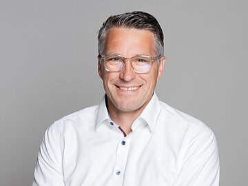 Business-Porträt eines lächelnden Mannes Mitte 40 mit weißem Hemd und Brille. 