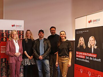 Gruppe mit 5 Personen, links und rechts danebenaufgestellte Werbewände zur Kampagne „Dein Platz ist hier. Werde Professorin!“ 