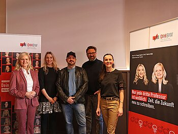 Gruppe mit 5 Personen, links und rechts danebenaufgestellte Werbewände zur Kampagne „Dein Platz ist hier. Werde Professorin!“ 