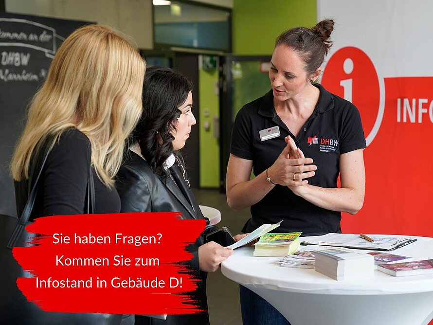 Eine Mitarbeiterin der DHBW Mannheim berät zwei Studierende an einem Infostand. Auf dem Tisch liegen Info-Flyer. Der eingeblendete Text lautet: Sie haben Fragen? Kommen Sie zum Infostand in Gebäude D!