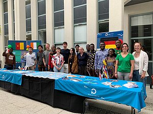 Studierende an einem langen Tisch mit unterschiedlichen Flaggen im Hintergrund.