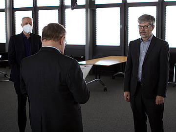 3 Mitarbeiter im Anzug in einem Konferenzraum zur Überreichung der Urkunde