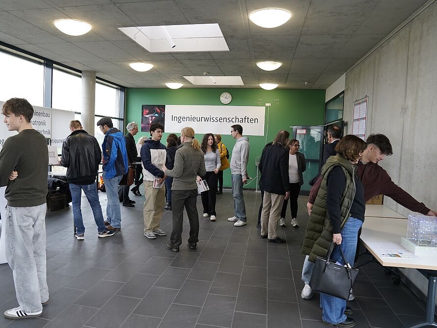 Menschen im Gespräch, im Hintergrund Plakate zu den einzelnen Studiengängen der Fakultät Technik.