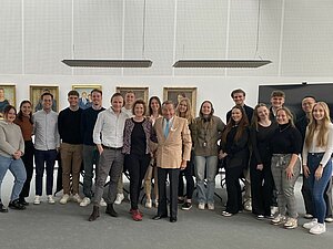 Gruppenbild der Studierenden bei der Firma Trigema, im Hintergrund Bilder mit Personen des Familienunternehmens. 