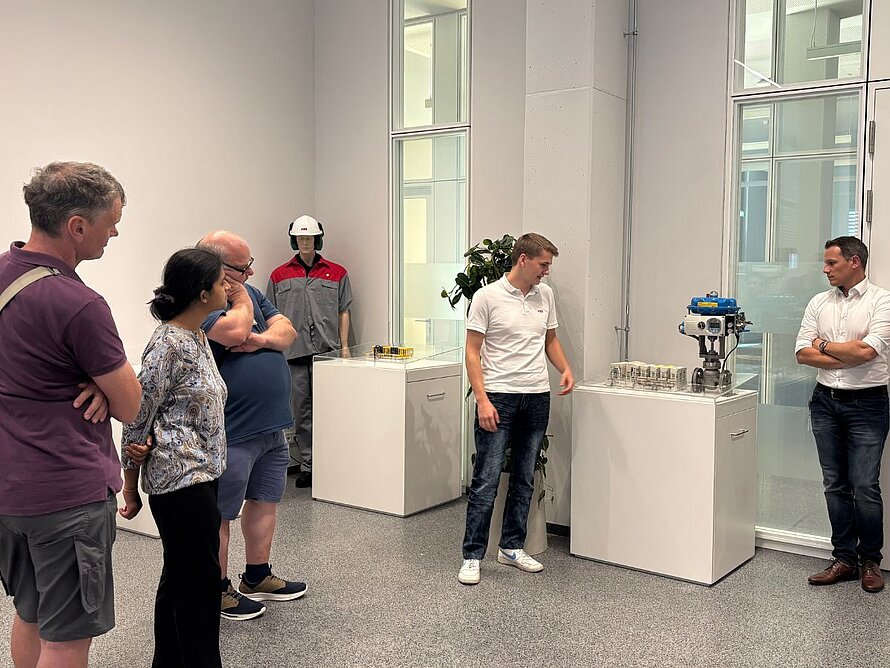 Gruppe von 5 Menschen im Ausstellungsraum der ABB, wo ein Mann in der Mitte die Ausstellungsstücke erklärt.