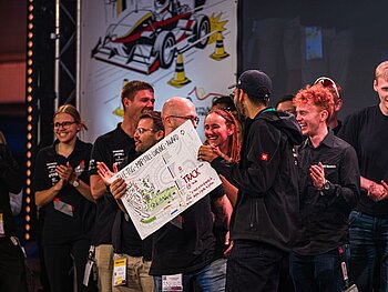 Gruppe mit 10 lachenden und klatschenden CURE-Mitgliedern auf einer Bühne. Einer davon hält eine Art Urkunde in der Hand, auf der eine Straßenkarte sowie der Namen des Awards abgebildet sind. 