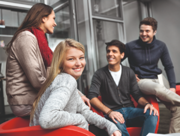 4 Studierende sitzen locker auf Sesseln, die vordere Studierende blickt lachend in die Kamera, die anderen lachen miteinander.