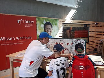 Vater mit seinen 2 Söhnen puzzelt am BUGA-Stand der DHBW Mannheim die Orte, Flüsse und Straßen an die richtige Stelle. 