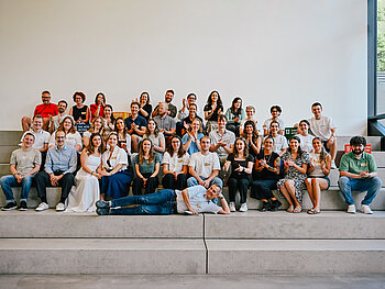 Gruppenfoto der 6 Studierendenteams der DHBW sitzen zusammen auf grauen Steinblöcken