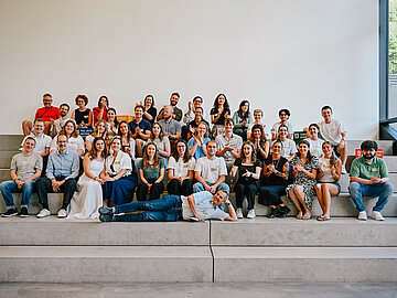 Gruppenfoto der 6 Studierendenteams der DHBW sitzen zusammen auf grauen Steinblöcken