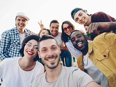 Selfie mit einer diversen Gruppe bestehend aus 8 in die Kamera lachenden Personen im Studierendenalter