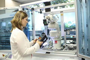Weiß gekleidete Studentin (von der Seite zu sehen) bedient einen 6-Achs-Roboter im Labor Handhabungstechnik des Studiengangs Maschinenbau an der DHBW Mannheim