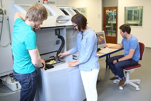Zwei Studenten und eine Studentin (von der Seite zu sehen) bedienen einen 3-D-Drucker in der studentischen Werkstatt im Studiengang Maschinenbau an der DHBW Mannheim