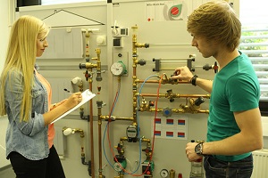 Ein Student bedient ein Heizungssystem im Labor  Versorgungs- und Energiemanagement der DHBW Mannheim, eine Studentin (beide von der Seite zu sehen) macht Notizen 