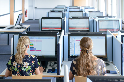 Zwei Studentinnen sitzen an je einem PC und machen Eignungstest des Programms Dual Assessment