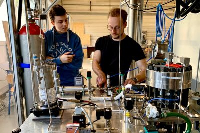 Zwei Studierende mit einem Elektrochemischen Verdichter im Wasserstoff-Labor der DHBW Mannheim, neben ihnen eine Wasserstoff-Flasche.