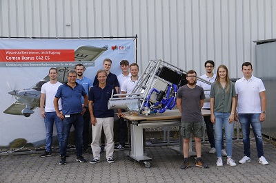 Gruppenbild am Campus Eppelheim: 9 Studierende und 2 Lehrende neben dem Versuchsaufbau des Brennstoffzellensystems für die Luftfahrt.  