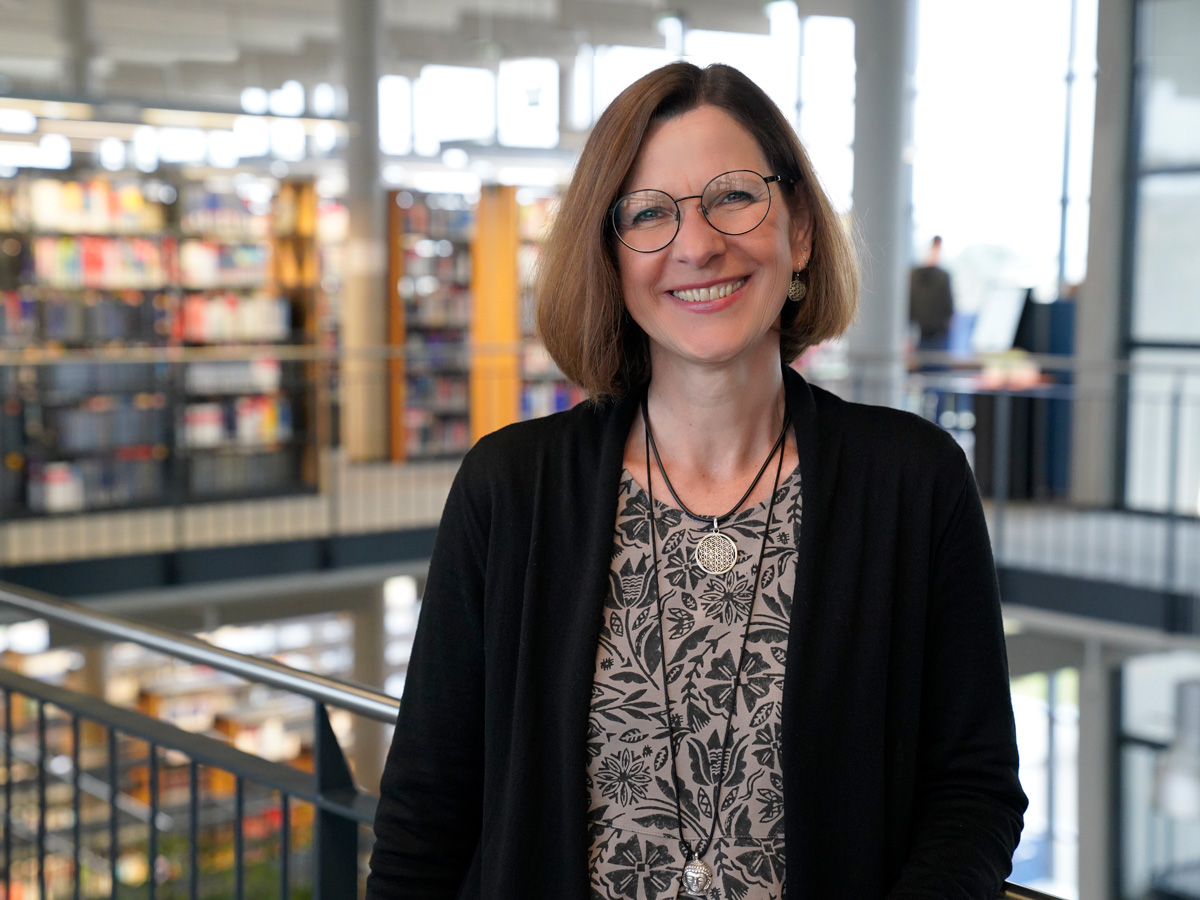 Verwaltungsdirektorin Angelika Neckermann lächelnde Frau vor Bibliothek-Innenraum, unscharf