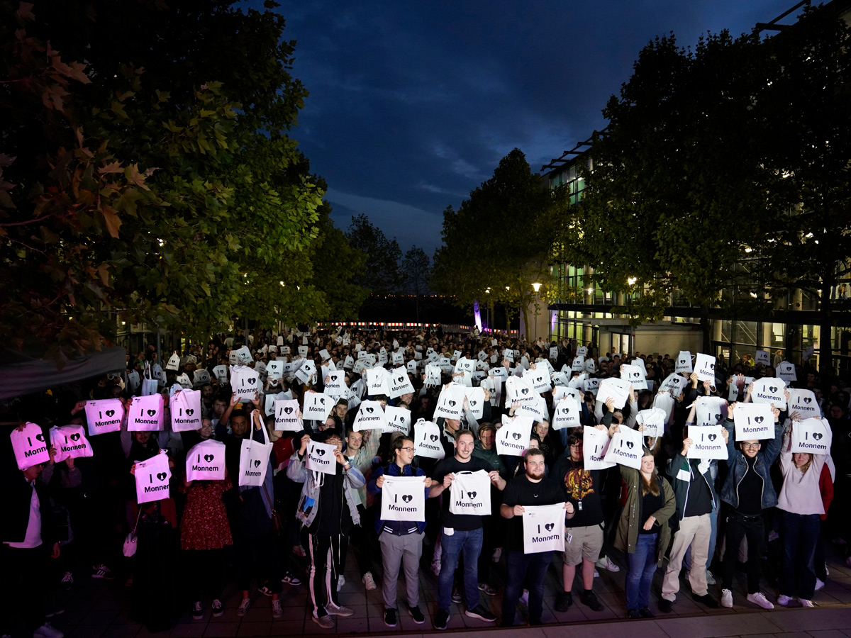 Gruppe von Studierenden auf dem Außengelände der DHBW Mannheim hält Beutel mit der Aufschrift I love Monnem hoch.