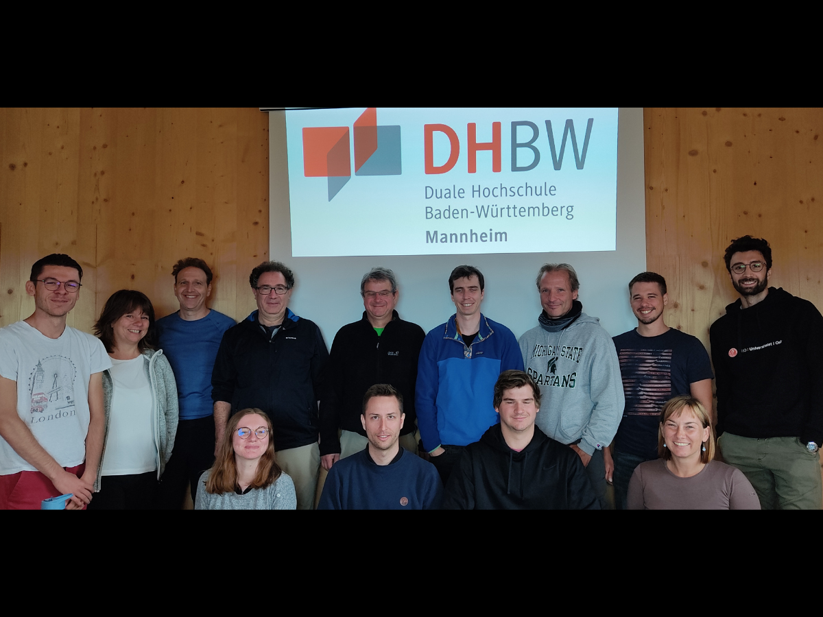 Gruppenbild Teilnehmer*innen Klausurtagung in der Österreichischen Kaltenberghütte, dahinter das auf eine Leinwand projizierte DHBW-Logo
