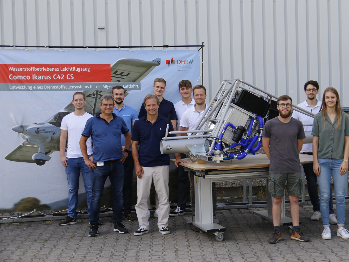 Gruppe Studierender und 2 Lehrende, in der Mitte der Versuchsaufbau eines Brennstoffzellensystems für ein Leichtflugzeug. 