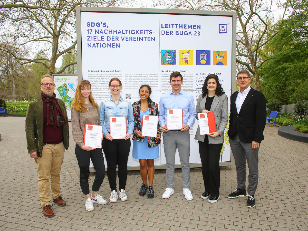 Gruppenfoto auf dem 5 Studierende mit Urkunden in der Hand zu sehen sind, dahinter eine Tafel der Bundesgartenschau 2023 zu den 17 UN-Nachhaltigkeitszielen.