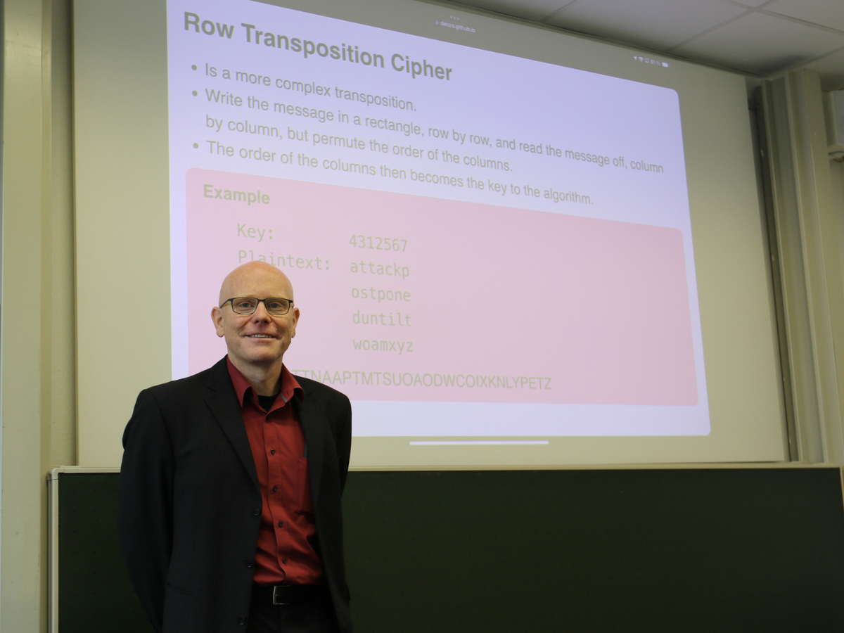 Porträt Prof. Eichberg vor einer an die Wand projizierten Präsentation zu Row Transposition Cipher.