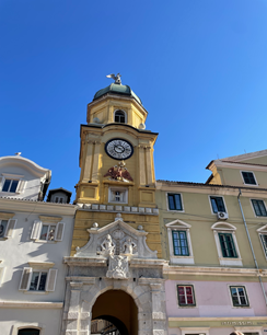 Altes Gebäude mit Turmuhr in Rijeka, darüber strahlend blauer Himmel.